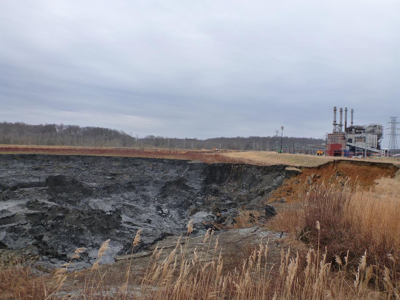 A massive coal ash pond at a power plant in North Carolina, showing eroded banks and gray-black coal ash waste next to the plant's smokestacks